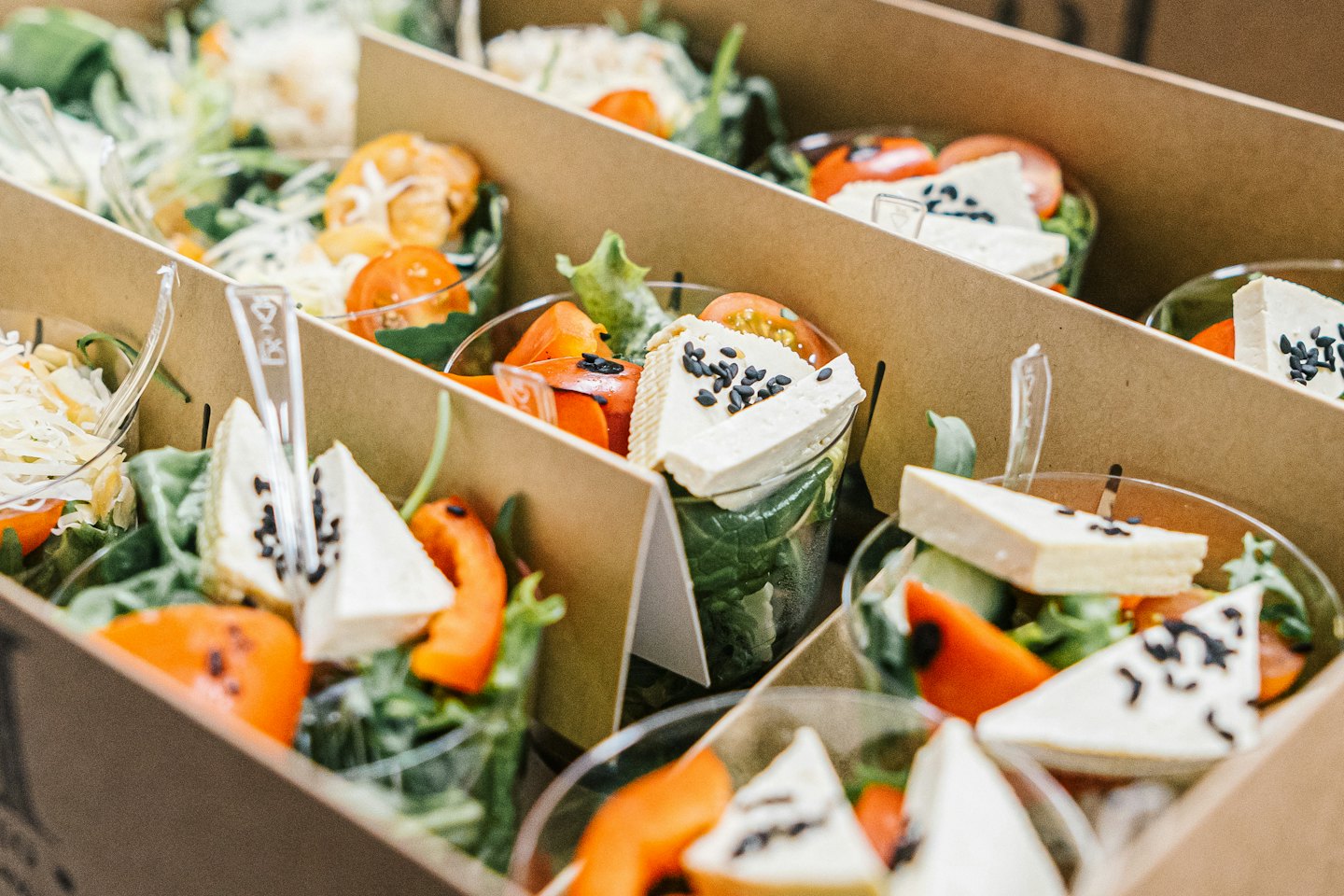 Individual catering portions of fresh salad in a cardboard tray.