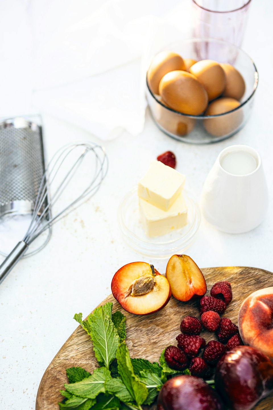 Baking ingredients laid out on a white countertop with eggs, milk, and fruit.