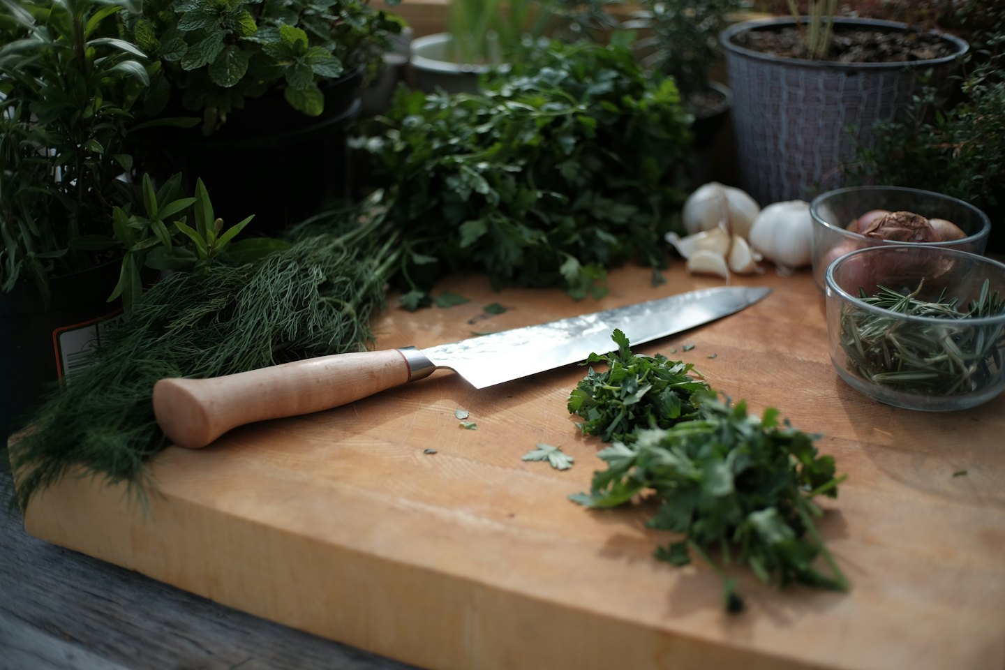 Herbs, garlic, and shallots on a wooden cutting board with a knife.